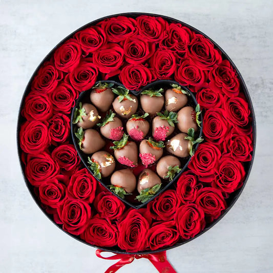 Caja redonda con rosas rojas vibrantes y un corazón de fresas bañadas en chocolate decoradas con oro comestible